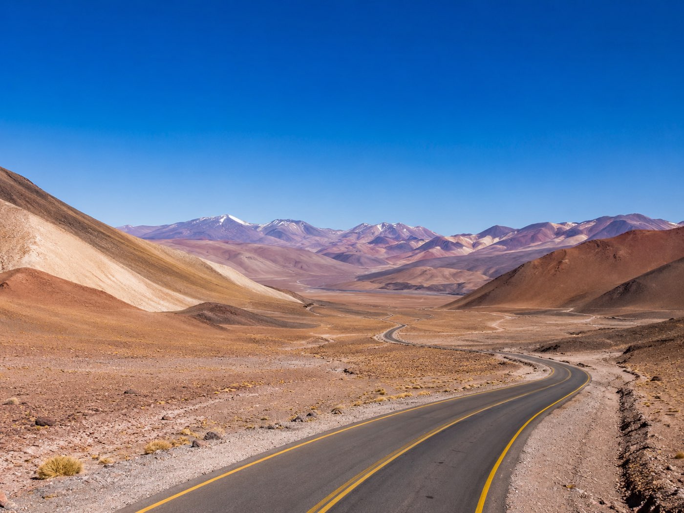 Corredor logístico pavimentado hacia la alta cordillera de Catamarca, con cumbres nevadas de fondo